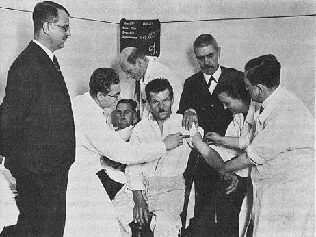 1934 photograph of malarial transfusion from one patient to a neurosyphilitic patient.  Dr. Wagner-Jauregg is in a suit on the right. 	 
